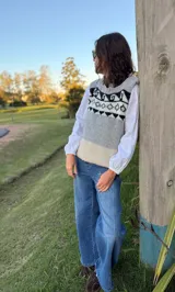 Chaleco tejido en mohair con diseño de guarda geométrica en la parte superior. Presenta una combinación de colores gris, blanco y beige, con cuello redondo y corte recto.