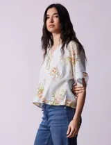 Blusa blanca estampada con flores azules, escote en V y mangas cortas amplias. Detalles de puntilla en escote y mangas.