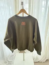 Buzo cropped de algodón color verde militar, con mangas ranglan y diseño estampado en el frente con motivos de besos y moños. Cuenta con elástico holgado en la cintura y los puños.