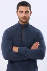 Buzo de punto color beige, con cuello alto y cierre frontal con cremallera y solapa de gamuza con botón. Presenta un tejido texturizado en el cuerpo y mangas lisas.