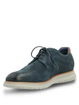 Zapato de estilo casual tipo derby, confeccionado en cuero azul marino con acabado gamuzado. Presenta detalles de costuras decorativas y perforaciones tipo brogue en los laterales, con un detalle en cuero color suela en el talón. Cuenta con cordones al tono y una suela de EVA flexible en color gris claro con tecnología de amortiguación.