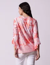 Blusa color salmón con estampado floral blanco, cuello redondo con abertura y mangas 3/4 acampanadas.