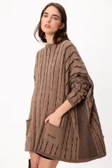 Sweater de punto con diseño de trenzas verticales, color crudo y camel, con bolsillos frontales y detalle de logo bordado. Presenta un corte holgado y mangas largas.