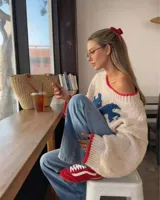 Sweater de tejido de punto grueso en color crema, con diseño de mariposas en color azul y detalles de terminación en color rojo en el cuello, puños y ruedo. Presenta un calce relajado, escote amplio y mangas largas.