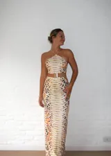 Vestido midi con estampado de piel de serpiente en tonos beige y marrón. Diseño con top halter y falda tubo con abertura lateral.