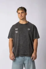Remera de algodón con efecto lavado ácido en color gris oscuro. Presenta cuello redondo, mangas cortas y múltiples estampados gráficos pequeños en el frente.