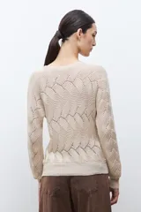 Sweater de punto color beige claro, con escote bote y tejido calado con diseño ondulado. Es de manga larga y corte recto.