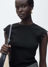 Camiseta de canalé color negro, con cuello redondo y diseño sin mangas. Presenta detalles de ojales metálicos en los hombros.