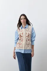 Chaleco tejido de punto color crema con bordados artesanales en color marrón, diseño sin mangas y cierre frontal con botones.