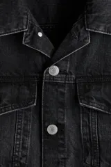 Campera trucker de denim rígido en color negro, con cuello camisero, cierre frontal de botones metálicos, bolsillos con solapa en el pecho y bolsillos laterales.