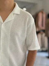 Camisa de manga corta negra con tejido texturizado tipo red, cuello camisero y cierre frontal con botones.