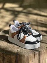 Zapatillas urbanas de cuero sintético color blanco, con puntera y talón en negro, laterales en marrón y cordones negros.