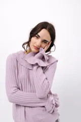 Buzo de tejido acanalado color lila, con cuello redondo decorado con dos volados y mangas largas con tres volados pequeños en los puños.