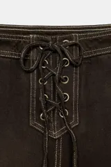 Jeans de tiro alto con pernera recta, confeccionados en denim color marrón oscuro con costuras en contraste. Presentan un diseño frontal con cordones ajustables y bolsillos laterales.