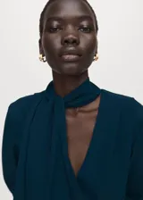Vestido corto de color verde oscuro, con escote en V, mangas largas y detalle de lazo integrado al cuello. Presenta un diseño ajustado en la cintura con fruncidos laterales en la falda.