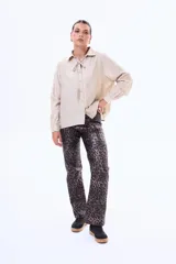 Camisa negra de corte clásico con cuello camisero y detalle de lazo ajustable en el cuello. Presenta cierre frontal con botones y mangas largas con puños abotonados.