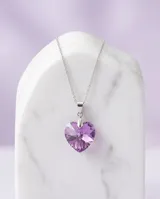 Collar de plata con cadena fina y dije en forma de corazón de cristal violeta tornasolado. Incluye aros haciendo juego con el mismo diseño de corazón.