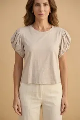 Remera de algodón color beige, de cuello redondo y mangas cortas abullonadas tipo globo con fruncidos en los hombros.