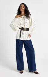 Sweater de punto color blanco con diseño geométrico calado. Presenta un amplio escote barco, mangas largas con volumen sutil y cintura ajustable mediante lazo frontal con terminaciones metálicas. Los puños y el bajo son acanalados.