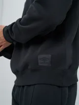 Buzo de felpa bordó, estilo relaxed, con cuello redondo y mangas raglán. Presenta puños y dobladillo acanalados, y una pequeña etiqueta con el logo de Umbro en el lateral inferior.