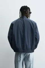 Cazadora bomber ligera de tejido técnico color verde oliva, con cuello, puños y bajo en rib elástico. Presenta cierre frontal de cremallera y bolsillos de vivo en la cadera.