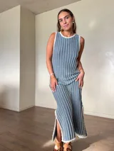 Vestido largo de punto sin mangas, color gris con rayas verticales blancas y destellos de lurex dorado. Presenta cuello redondo y abertura lateral en el dobladillo.