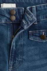 Jeans de denim de algodón con leve stretch, tiro alto, corte ajustado hasta la rodilla y acampanado desde la rodilla al bajo. Presenta cierre y botones frontales, y solapas de bolsillo decorativas con botón en la parte delantera.