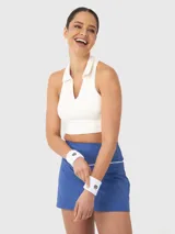 Conjunto deportivo compuesto por un top corto tipo polo sin mangas en color blanco y una pollera deportiva azul con cintura alta y detalle de vivo en contraste.