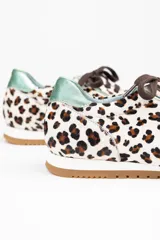 Zapatillas de estilo running con estampado animal print de leopardo sobre fondo blanco. Presentan detalles en piel verde tornasolada en la parte trasera y lengüeta, cordones oscuros y suela de goma dentada con cuña interna.