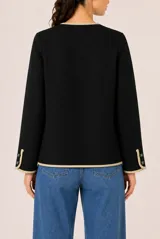 Saco de punto negro con ribetes en color beige, cuello redondo, cierre frontal con botones y dos bolsillos delanteros con solapa.