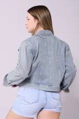Campera de jean de lavado celeste claro, con diseño clásico de cuello y botones metálicos. Presenta detalles de pequeños brillos o tachas plateadas sobre la tela, especialmente visibles en los bordes de los bolsillos y costuras.