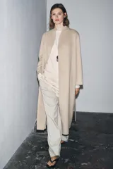 Abrigo largo de corte minimalista confeccionado en mezcla de lana, con diseño de solapas integradas, manga larga y cinturón ajustable del mismo tejido.