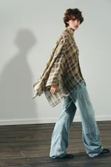 Capa corta con estampado a cuadros en tonos mostaza, marrón y blanco. Presenta un cuello redondo y mangas amplias tipo murciélago. Incluye un lazo o foulard integrado en el cuello para anudar.