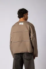 Buzo oversize de corte boxy, confeccionado en algodón rústico de alto gramaje en color beige. Presenta cuello redondo con borde crudo, mangas largas y una estampa frontal con el texto VCP delimitado por líneas horizontales blancas.