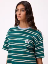 Remera de corte holgado con diseño de rayas horizontales en tonos beige, rosa y verde oliva. Presenta cuello redondo, mangas cortas y un bolsillo frontal pequeño con el logo de la marca.