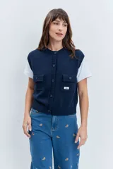 Chaleco de punto rojo con cierre frontal de botones, cuello redondo y dos bolsillos frontales con solapa. Presenta un diseño de tejido acanalado en los bordes y un pequeño parche decorativo en el pecho.