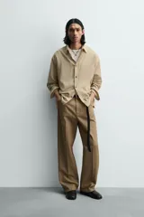 Camisa de hombre de manga larga, color beige con micro-estampado a cuadros en tonos marrones. Presenta cuello solapa abotonado (button-down), un bolsillo de parche en el pecho y cierre frontal de botonadura.