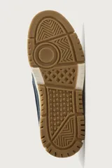 Zapatilla de básquet con cordones, diseño urbano de caña baja. Parte superior confeccionada en combinación de cuero sintético blanco y piezas de denim azul, con suela chunky de goma marrón y entresuela blanca.