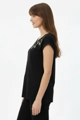 Remera de algodón negra, de corte holgado, con cuello redondo a la base y detalle de estampado floral en el hombro izquierdo.