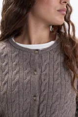 Saco de punto color tostado, con diseño de trenzas verticales en todo el cuerpo y mangas. Tiene cuello redondo y cierre frontal con botones pequeños.