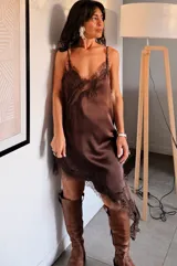 Vestido lencero de satén color blanco con detalles de encaje negro en el escote y el ruedo asimétrico. Presenta breteles finos y un corte fluido que se ajusta suavemente a la silueta.