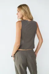 Top sin mangas color gris con rayas diplomáticas blancas, escote en V y detalle drapeado en el frente. Tiene cierre frontal.