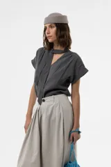 Camisa gris de corte relajado, con escote en V y lazo largo incorporado en el cuello. Mangas cortas con vuelta y frunce sutil en los hombros.