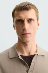 Polo de punto negro, manga corta, con cuello solapa y cierre frontal de tres botones. Presenta un calce regular y acabados en rib en mangas y ruedo.