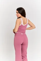 Conjunto deportivo de dos piezas en color rosa, compuesto por un top corto con tirantes finos y logo estampado, y un pantalón de corte acampanado con cintura alta.