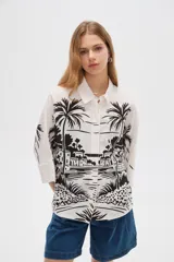 Camisa de viscosa de corte holgado, color blanco con estampado negro de paisaje con palmeras, cuello camisero y cierre frontal con botones.