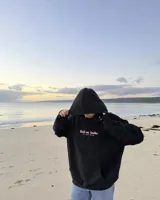 Canguro negro con capucha, de corte regular y confección en felpa suave, con estampa en la espalda de un personaje gráfico y texto "Kaboa Radio".