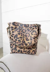 Cartera tipo bolso de hombro con diseño de estampado animal print de leopardo. Cuenta con una correa fija de longitud media y herrajes metálicos en tono bronce envejecido que conectan la correa con el cuerpo del bolso.