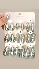 Set de nueve pares de aros tipo argolla y pendientes de metal plateado, con diversos diseños: gotas lisas, argollas gruesas lisas, argollas texturizadas con estrías, y diseños retorcidos.