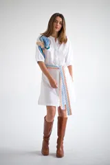 Vestido camisero corto color amarillo pálido con estampado floral en el hombro izquierdo y cinturón de tela con diseño geométrico.